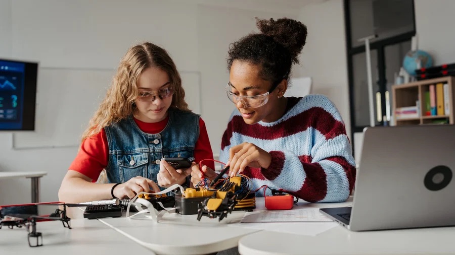 Two young people building electronics together at a laptop